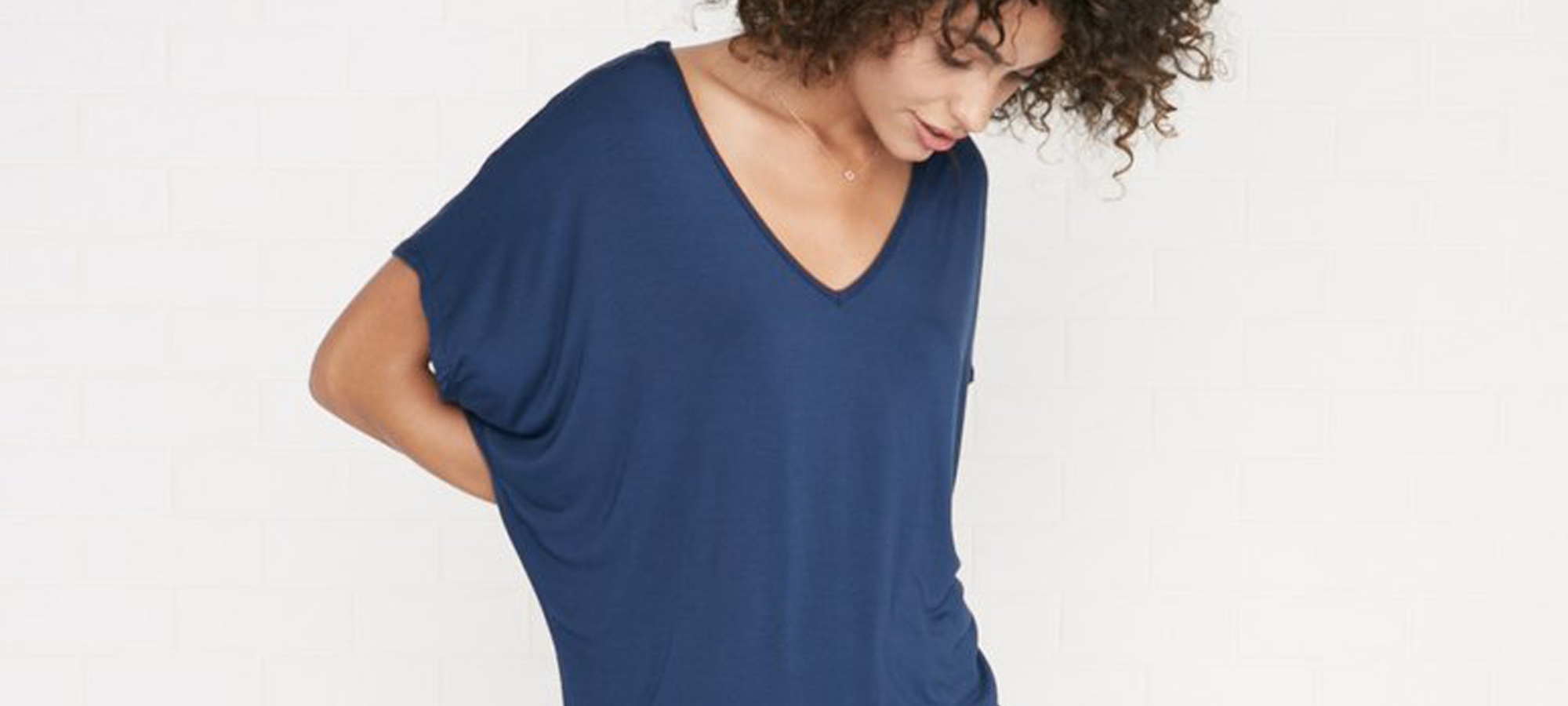 A woman with curly hair and a blue top looking down.