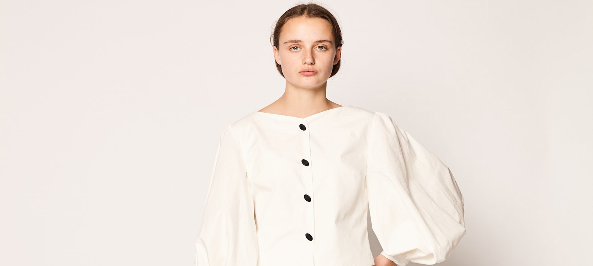 A woman with a cream blouse with puffy sleeves and black buttons.