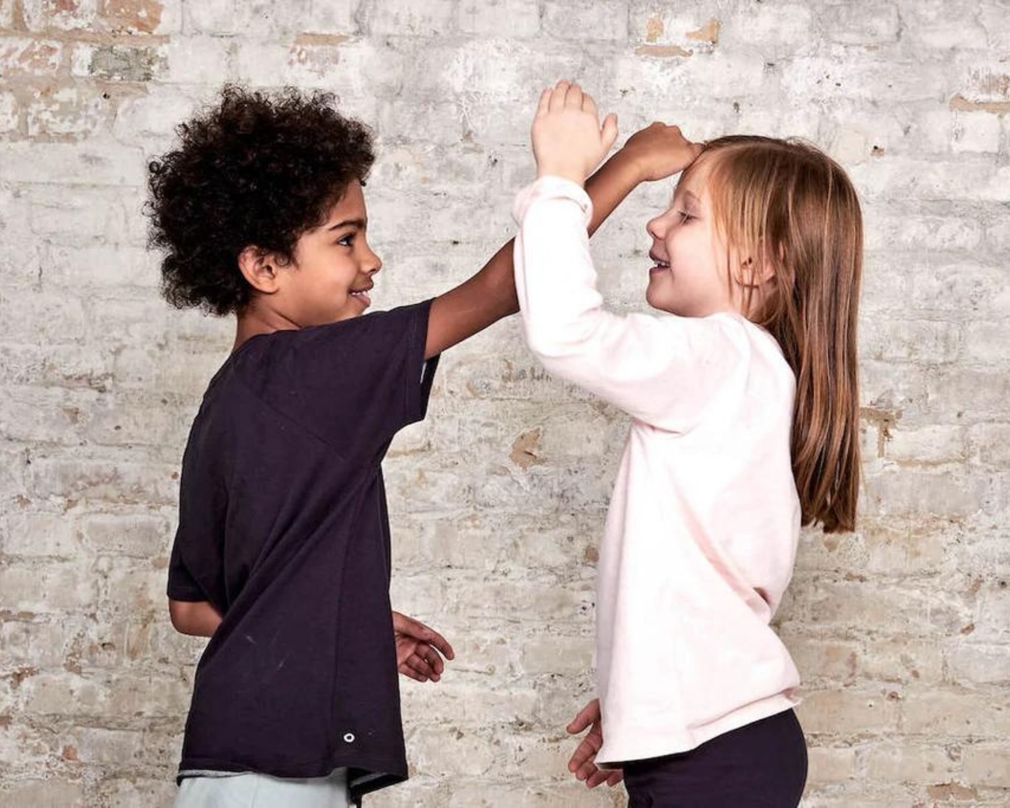 Two kids measuring eachother's heights, wearing neutral unisex children's clothing by Orbasics.