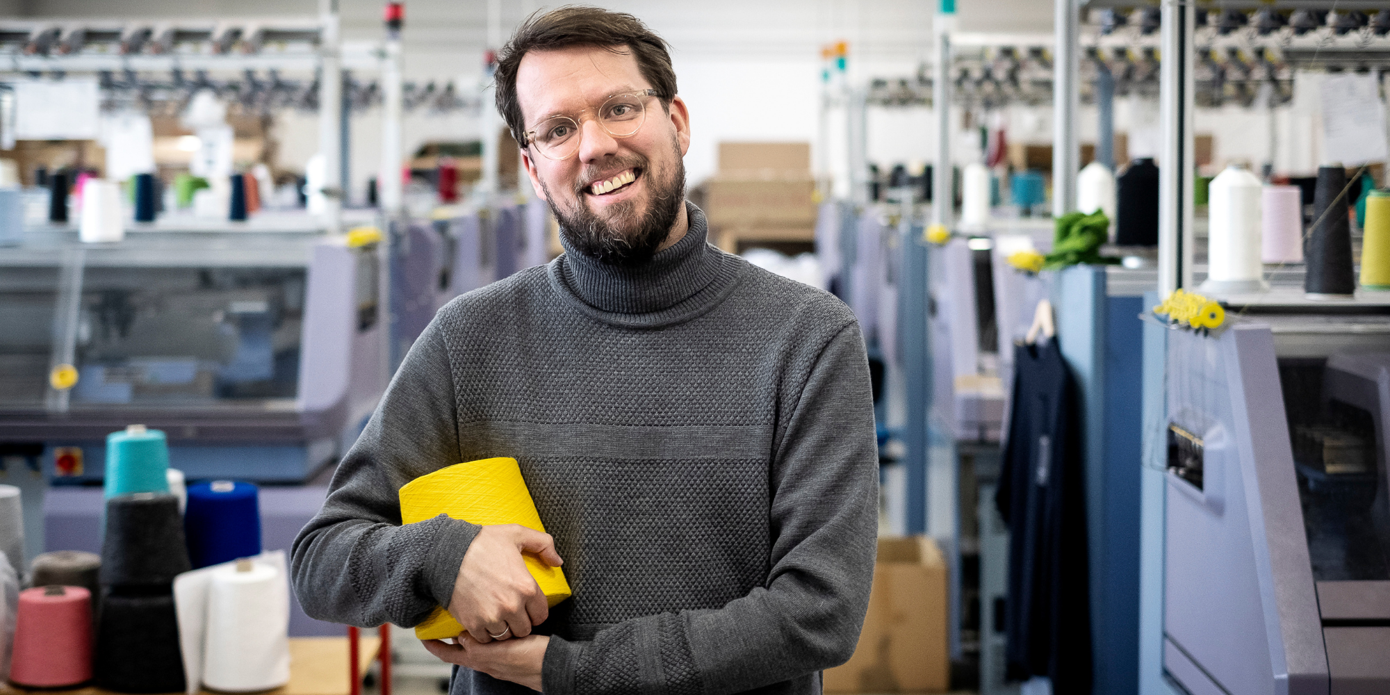 Merton the founder of Le Pirol holding a thread of yellow yarn and wearing a grey Le Pirol sustainable jumper