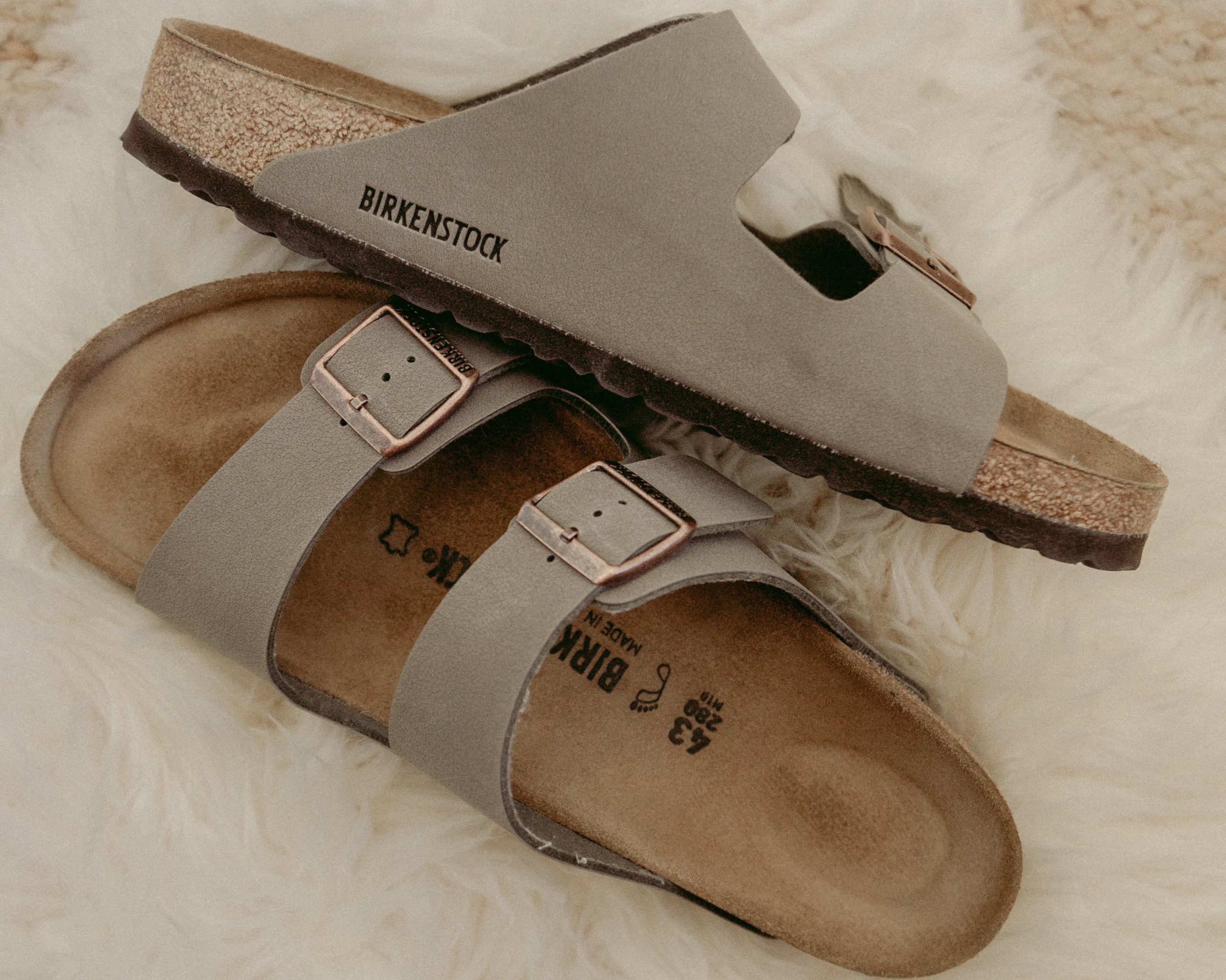 A pair of beige Birkenstocks laying on a fluffy white rug.