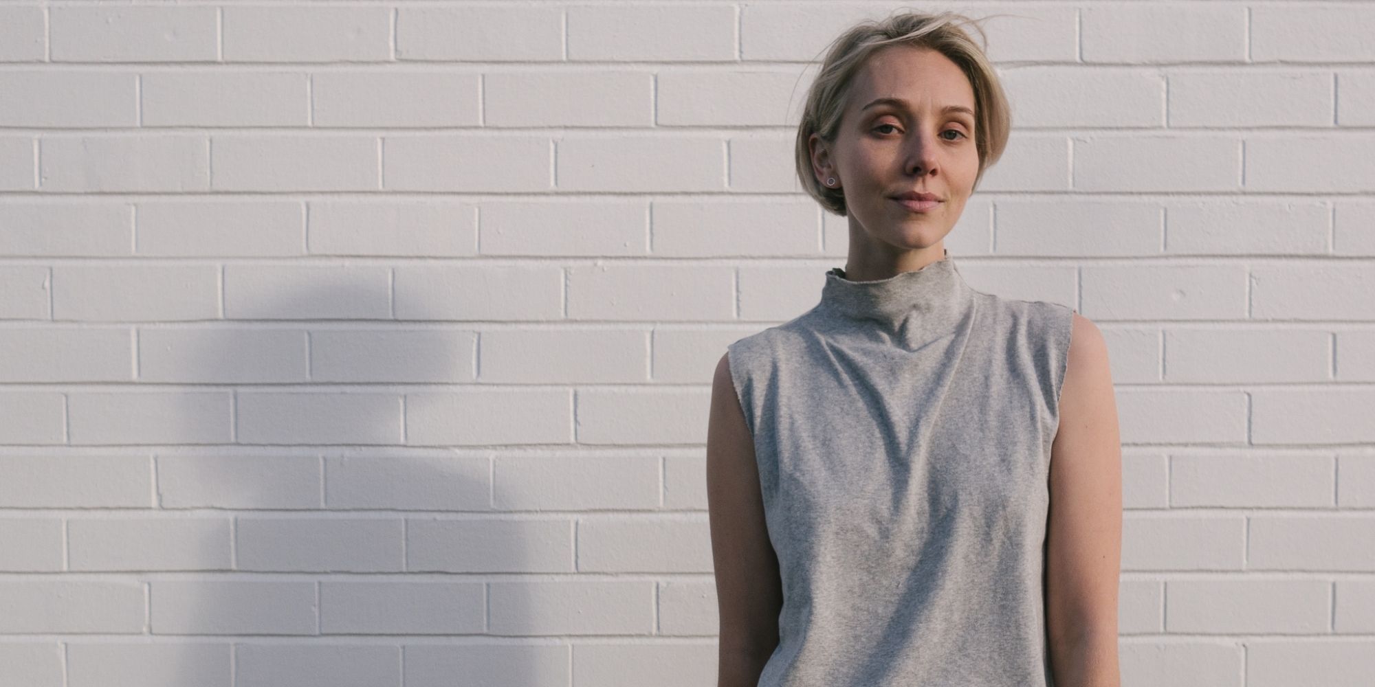 A.BCH founder Courtney Holm in grey singlet on white brick background