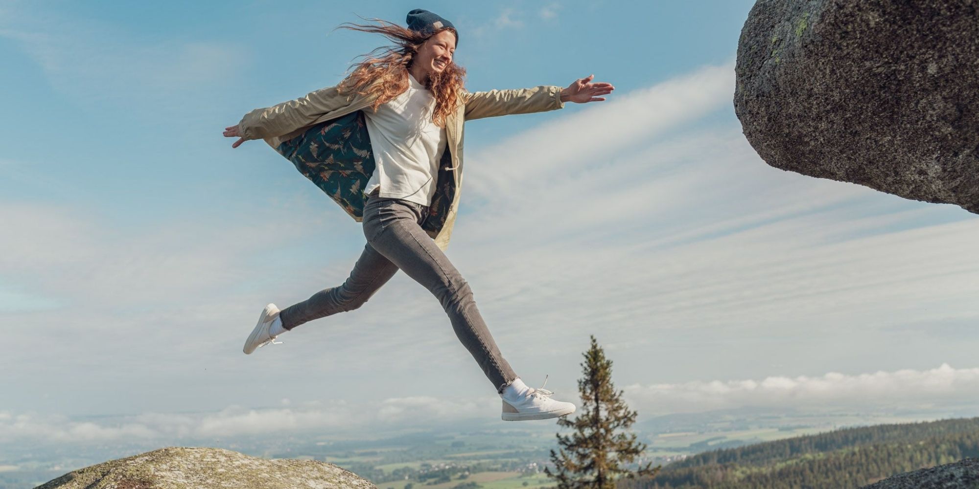 woman wearing sustainable sporty clothes by bleed jumping over mountain gap
