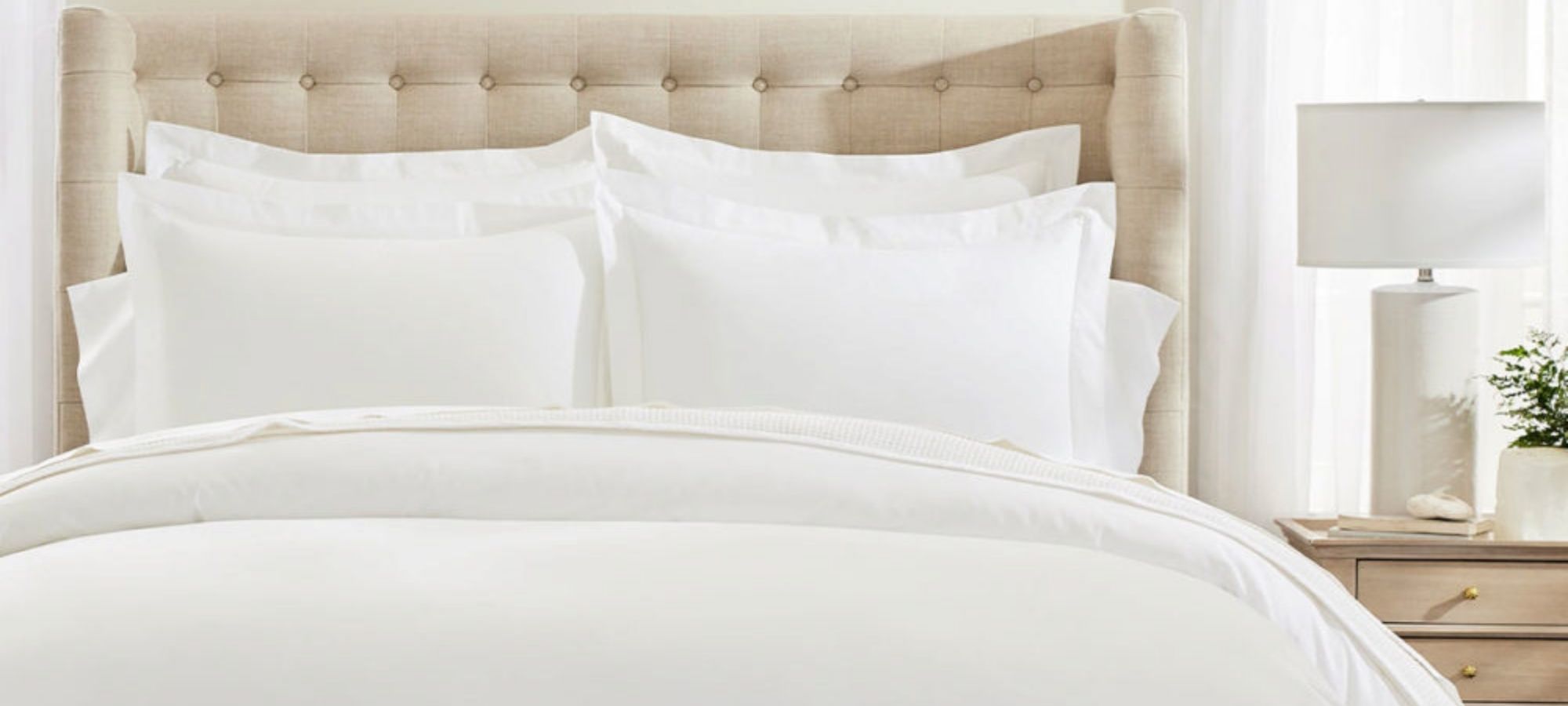Cropped view of a beige bed covered with organic white sheets by Boll & Branch.