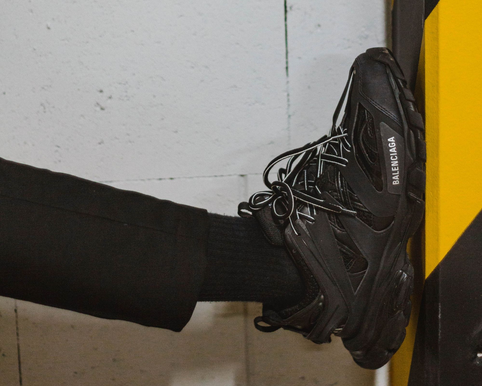 Someone pressing their black Balenciaga sneaker up against a caution taped wall.