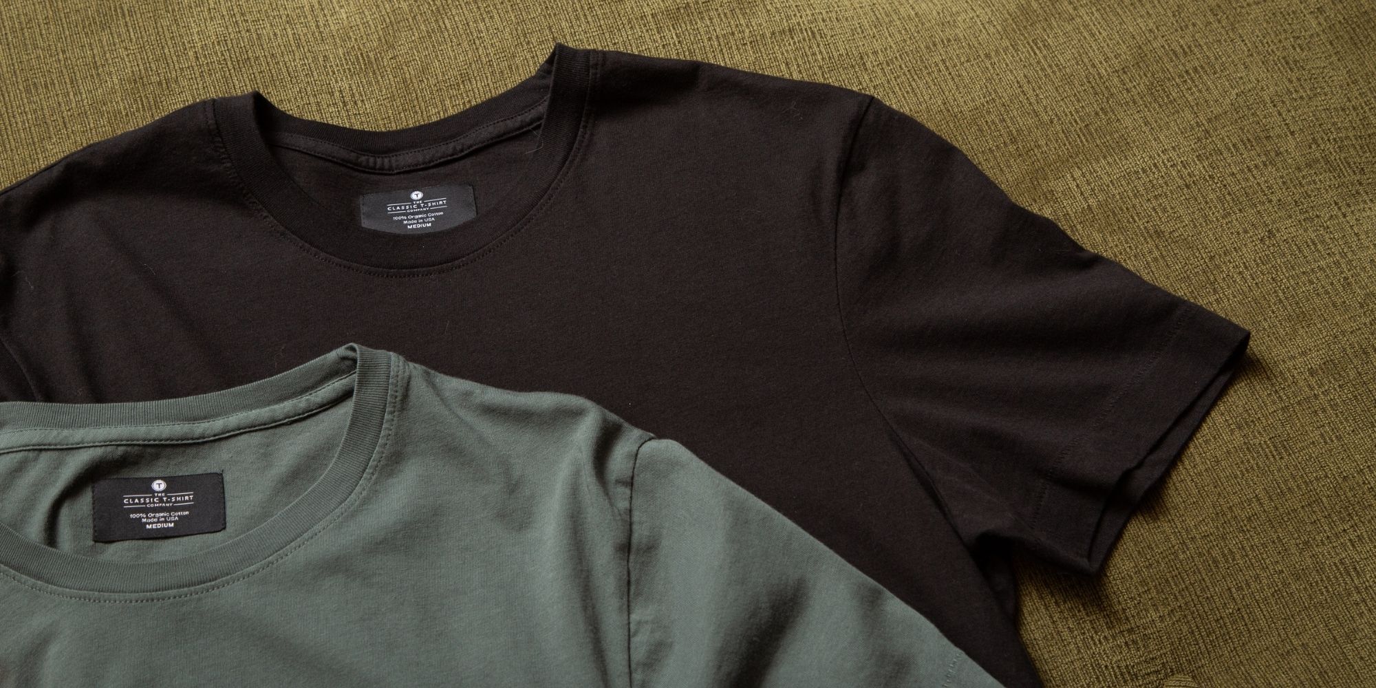 Cropped shot of a black and an olive green ethical tee made by The Classic T-Shirt Company.