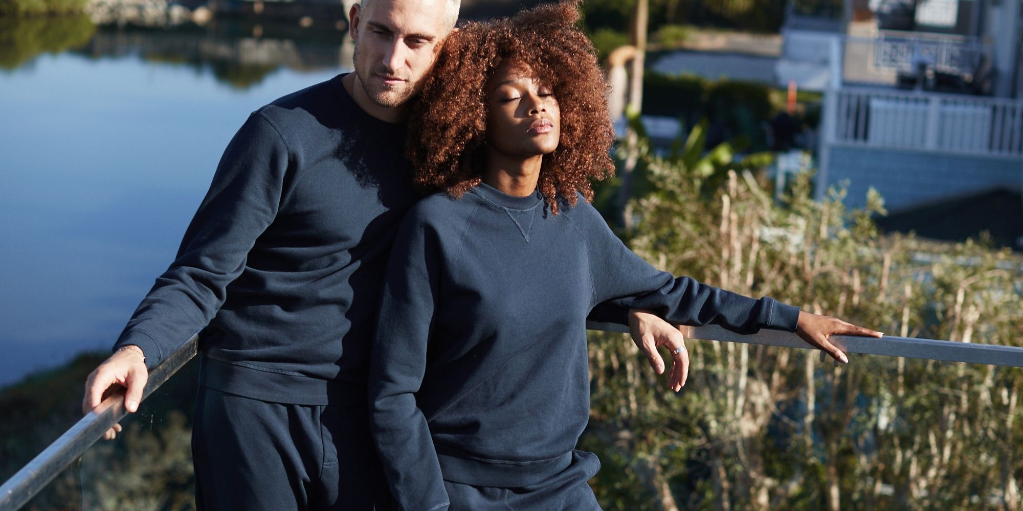 Two people embracing on a balcony while wearing navy blue ethical sweatshirts and joggers by The Classic T-Shirt Company.
