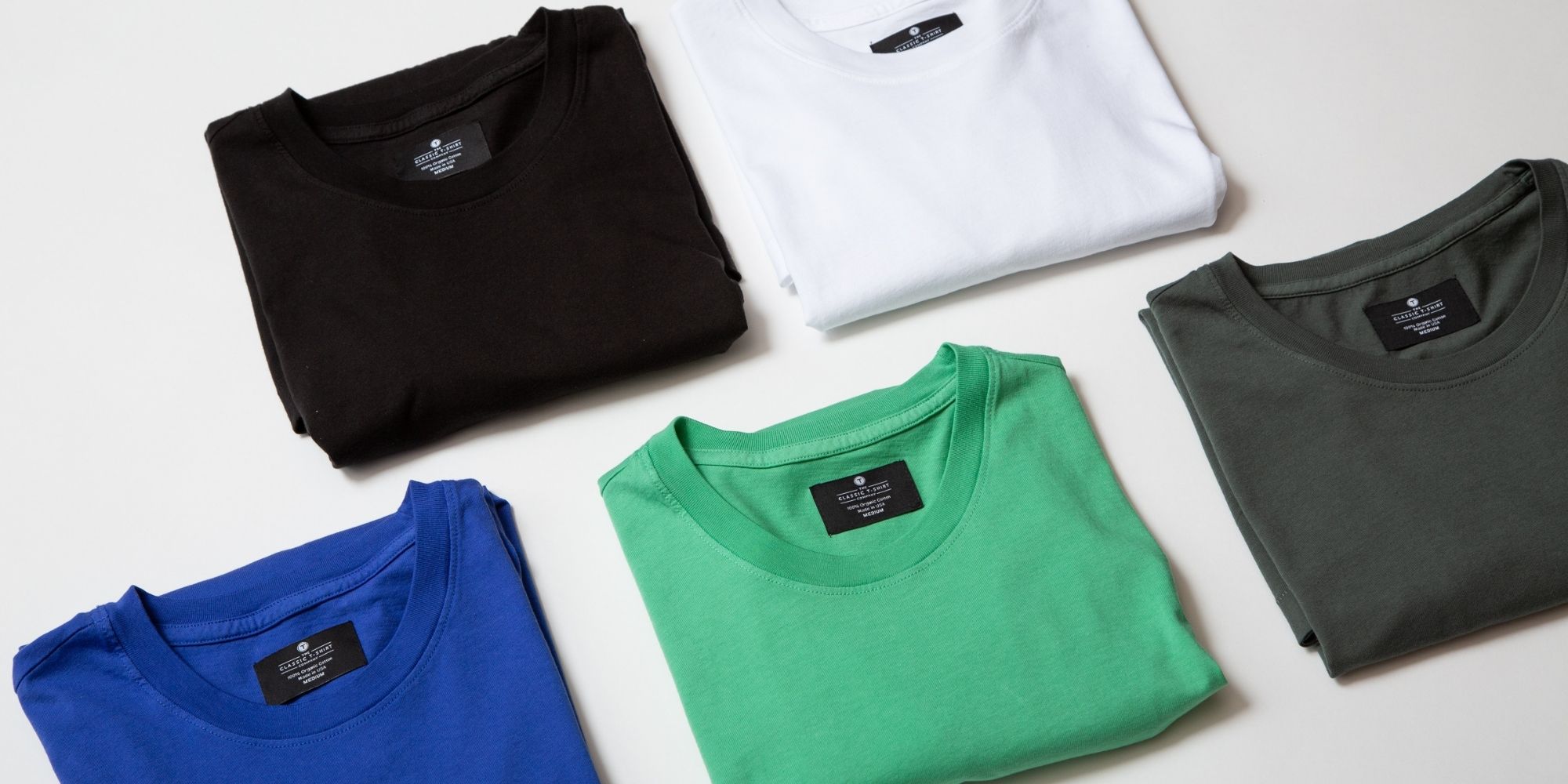 Five folded colourful shirts by The Classic T-Shirt Company laid out in a white background.