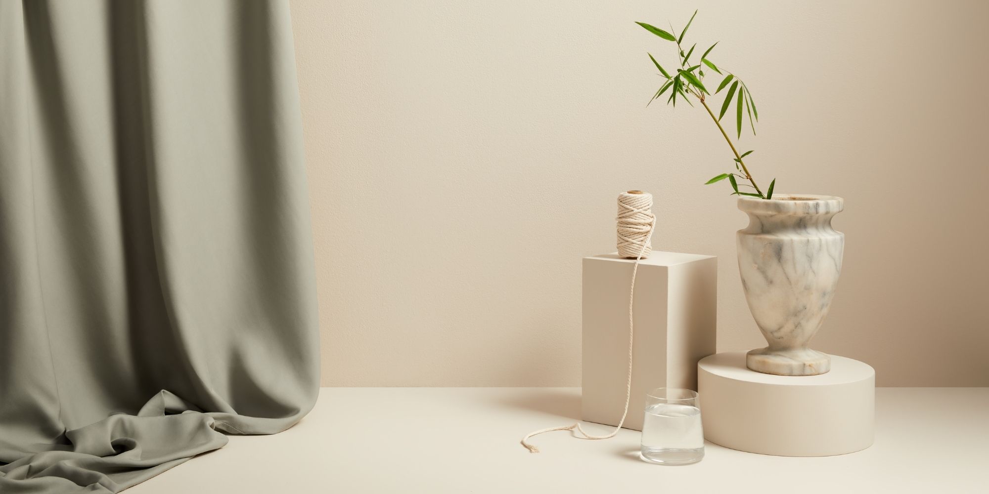 A bamboo plant and thread by a marble vase and draping of green sheets by ettitude.