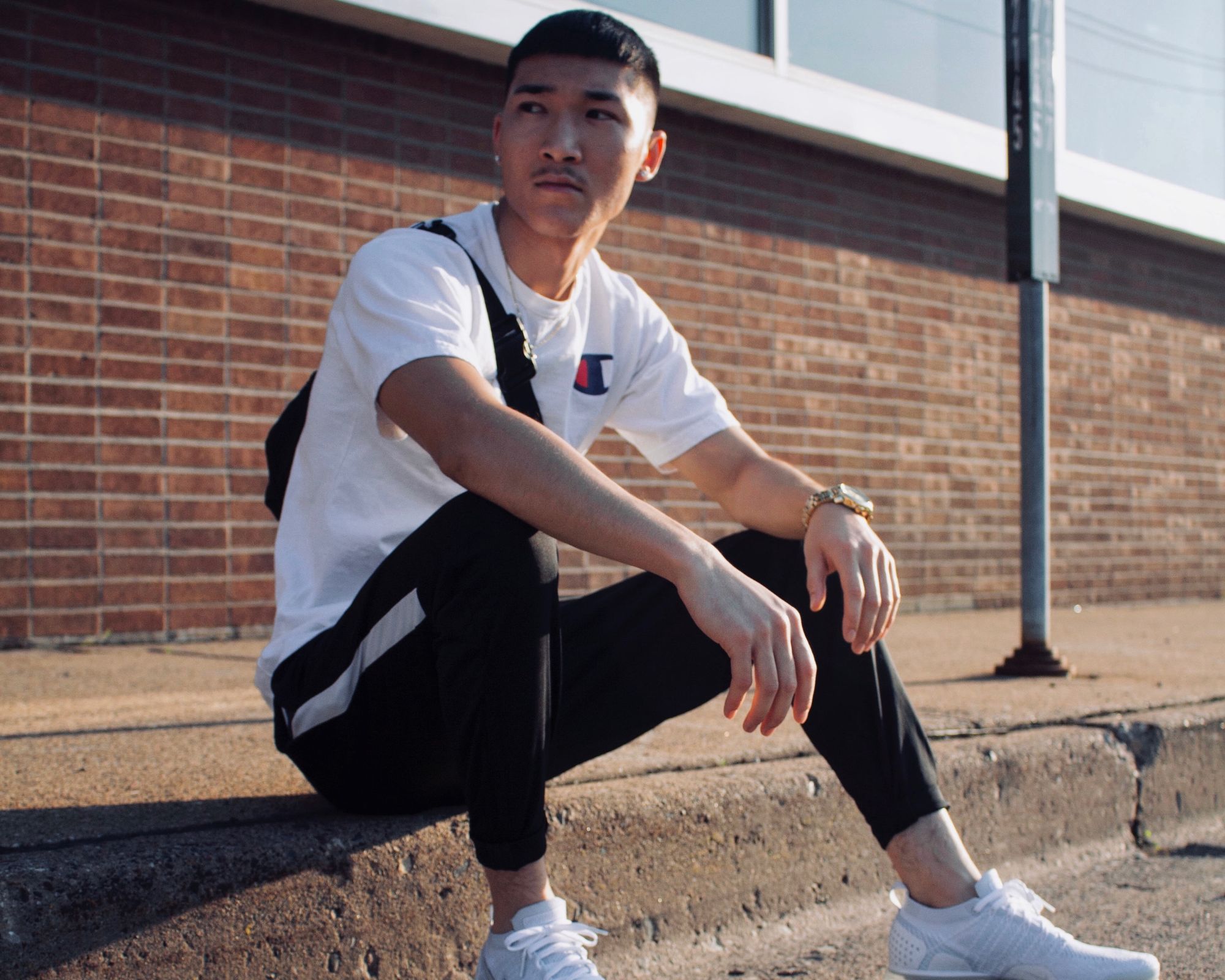Someone sitting on a curb wearing streetwear, including a white Champion t-shirt.