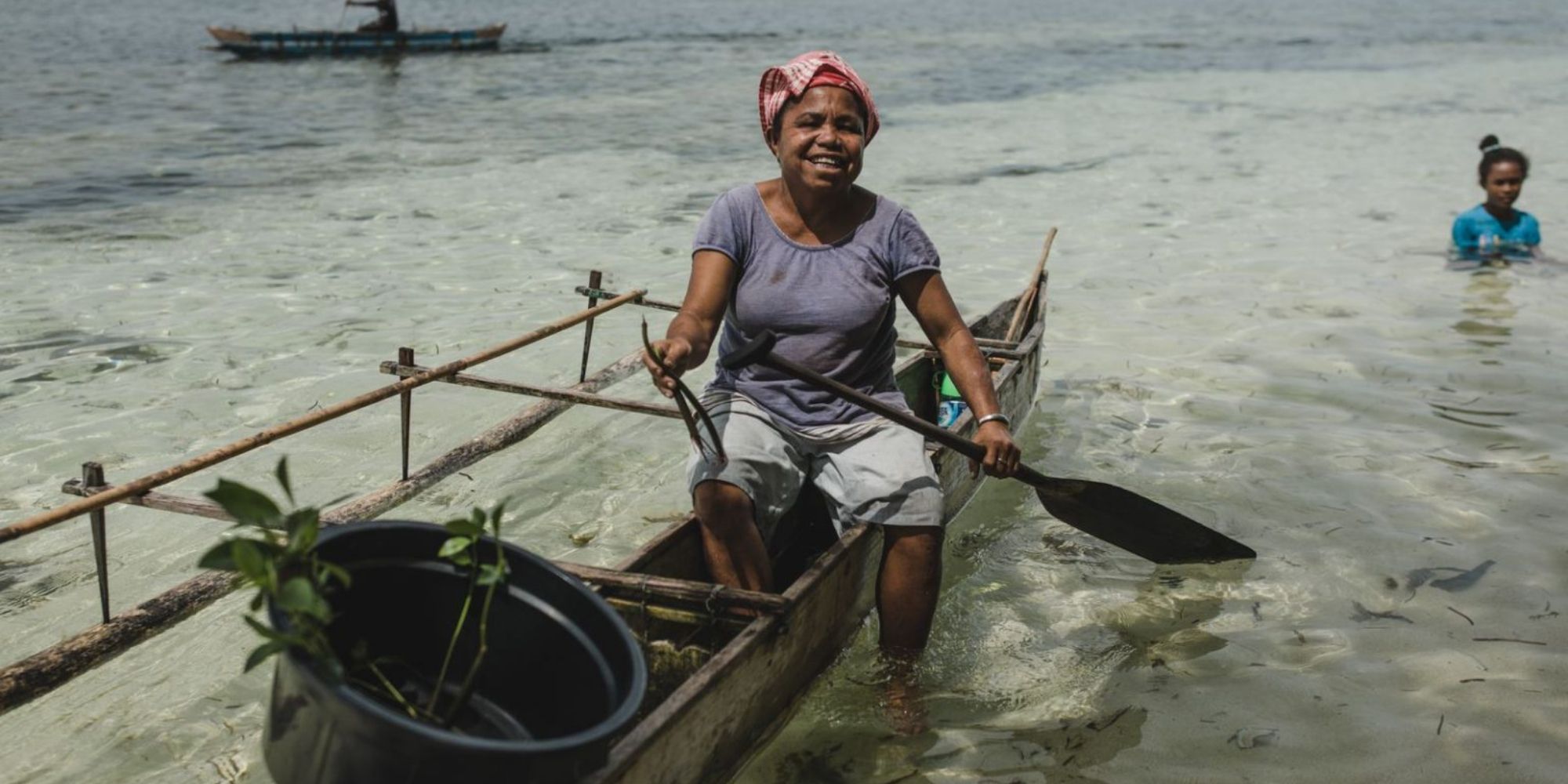 Someone sitting in a boat with a mangrove sapling smiling at the camera.