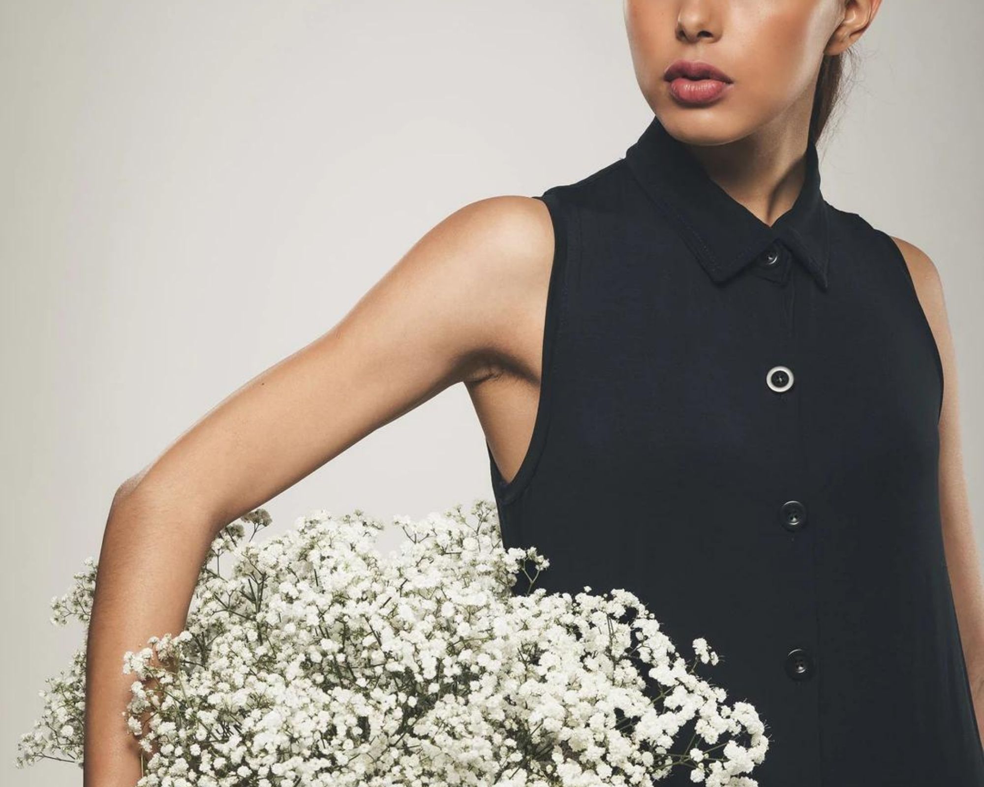 Someone wearing a black button up shirt dress by Organique and holding a basket of white flowers.