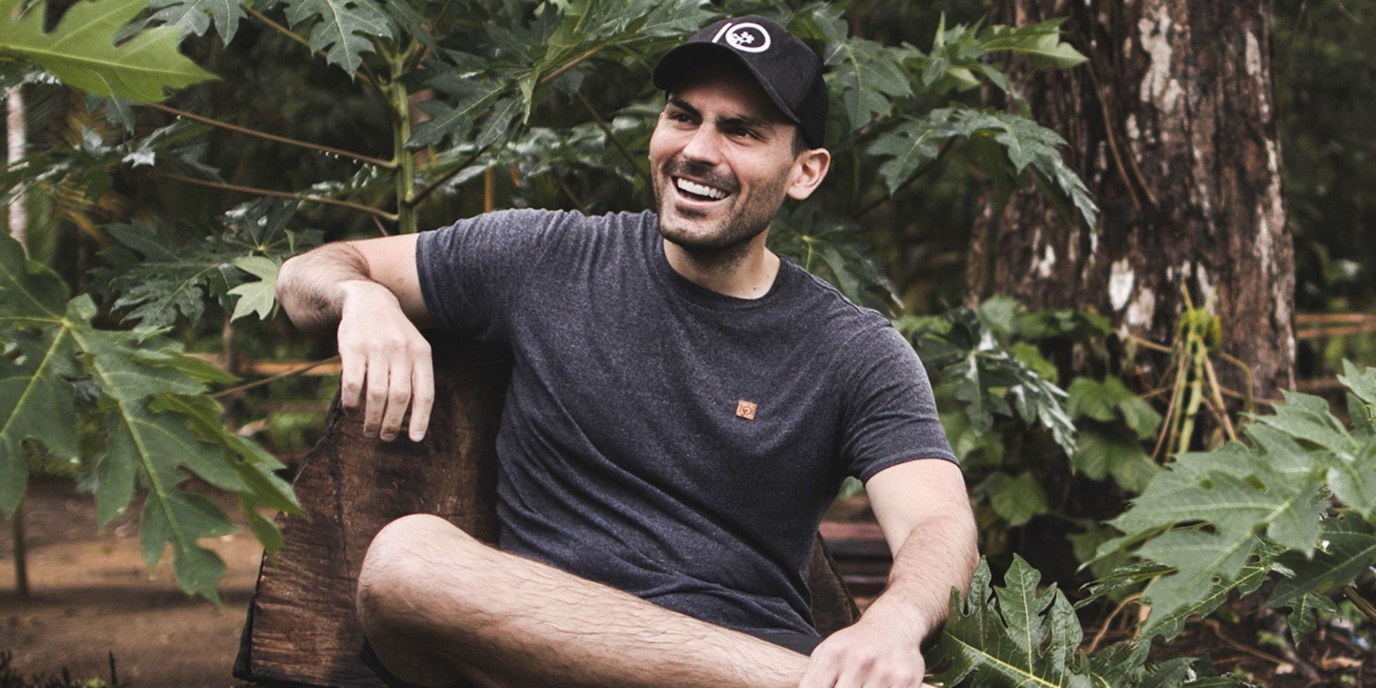 tentree co-founder and CEO Derrick Emsley sitting on a bench in a forest wearing a grey tentree shirt.