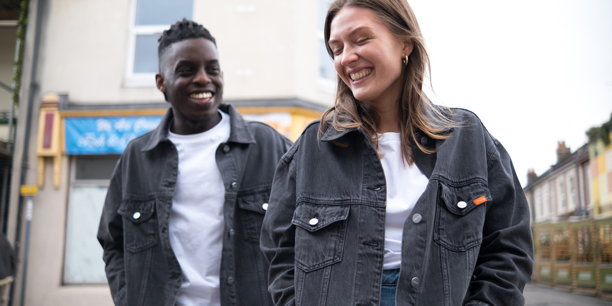 Two people smiling on the street wearing ethical and sustainable denim jackets by Yes Friends.