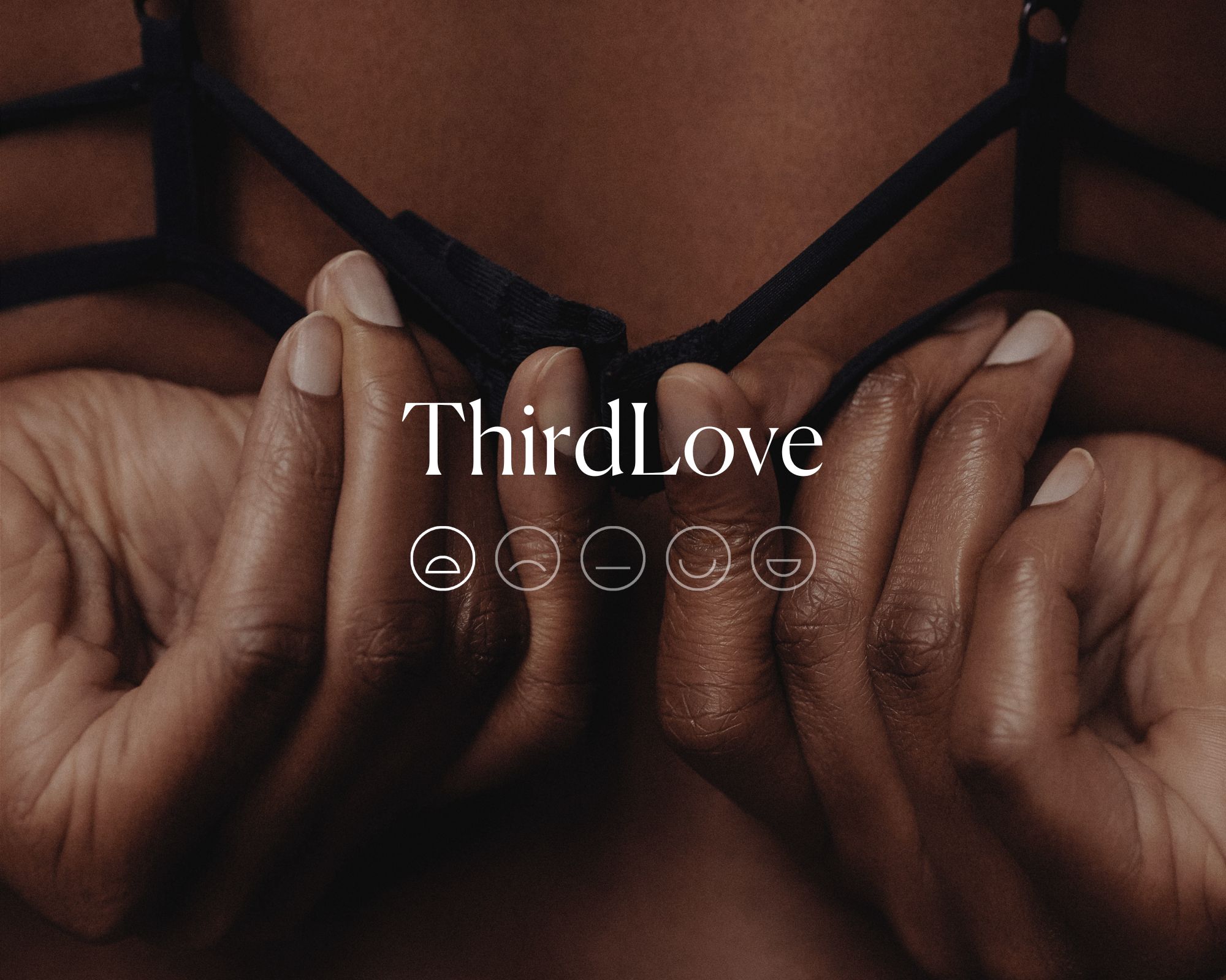 Close up of hands doing up a black bra clasp with the word ThirdLove and a sad emoji face highlighted in white.