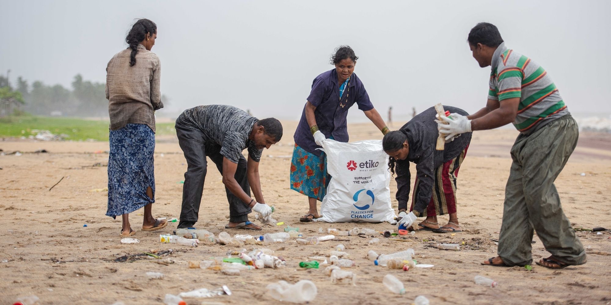 Five people working for Plastics For Change in India collecting plastic on the beach.