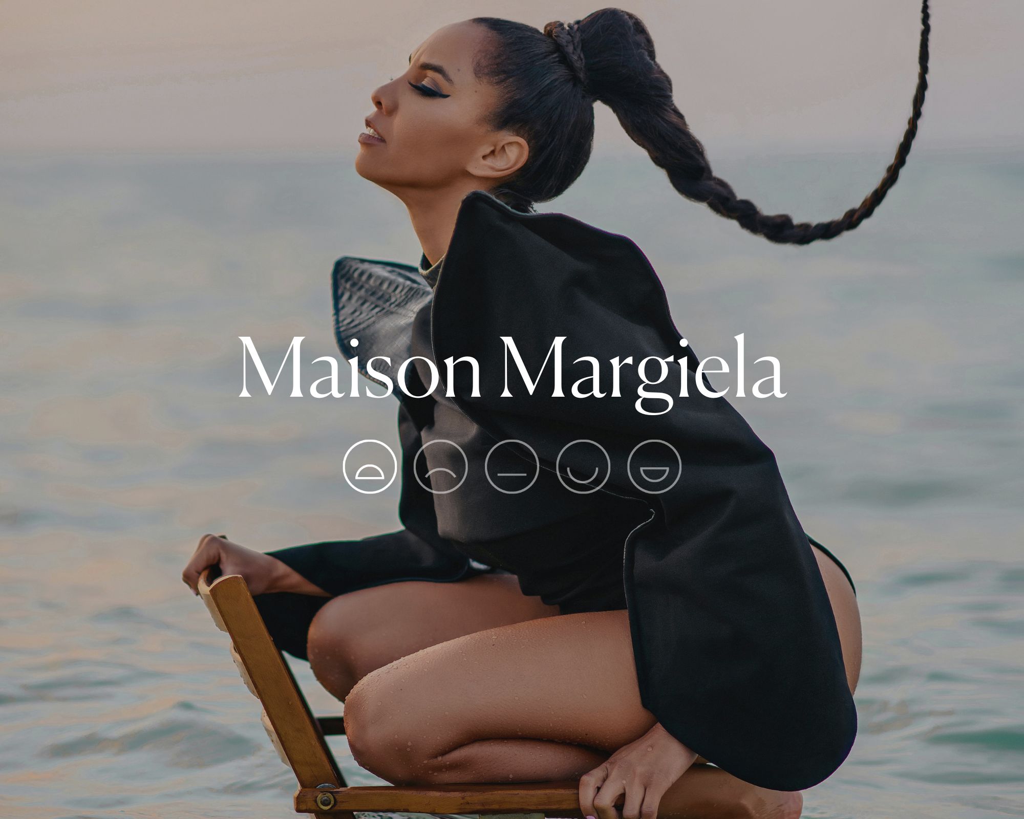 A black high fashion dress overlaid with white text reading Maison Margiela above a highlighted sad emoji face.