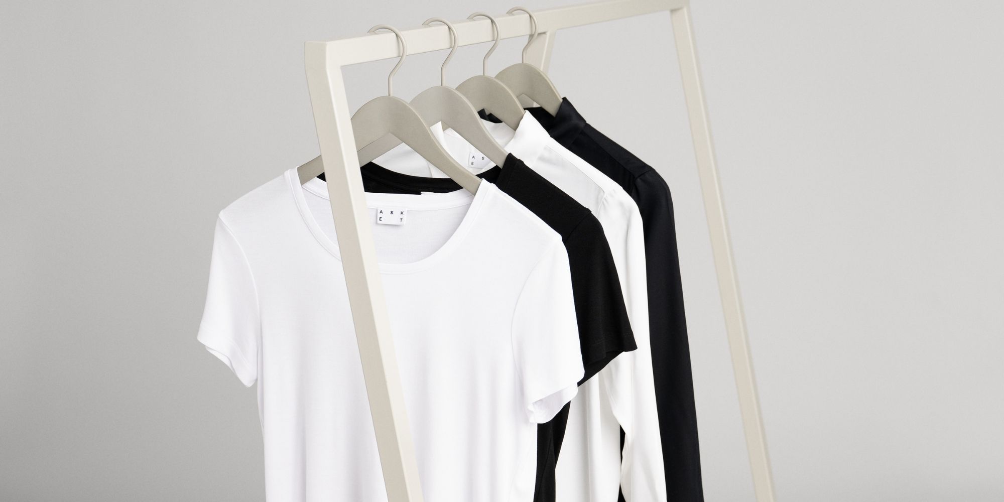 Two lyocell t-shirts and two lyocell button up shirts in black and white hanging on a railing, designed by ASKET.