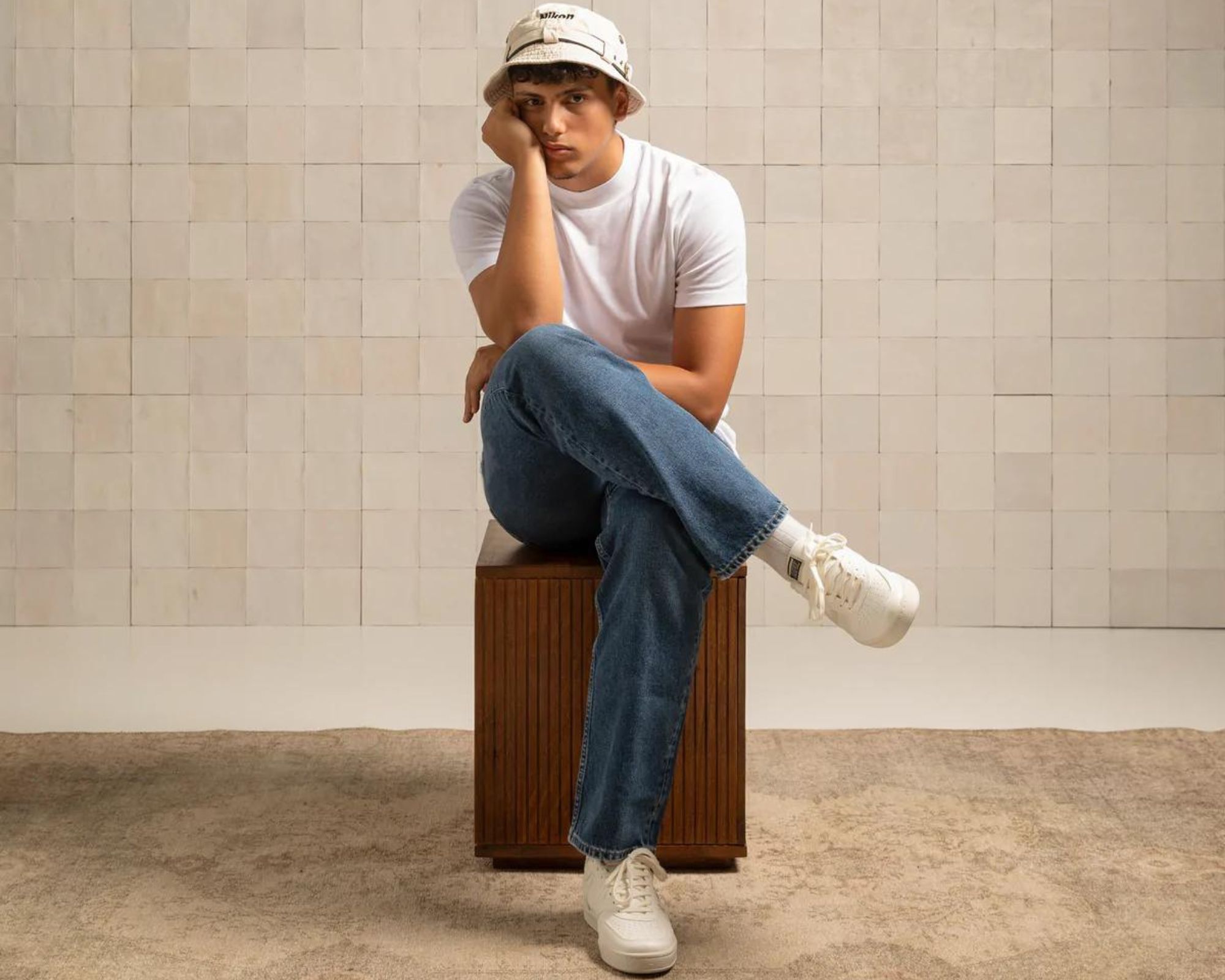 Someone sitting down with their legs crossed wearing a white tee, denim jeans, and white Flamingos' Life sneakers for men's spring fashion.