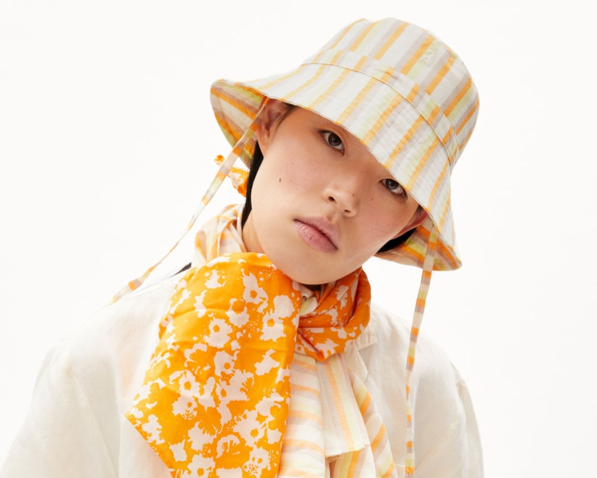 A white and yellow striped bucket hat with a chin strap made by Armedangels.