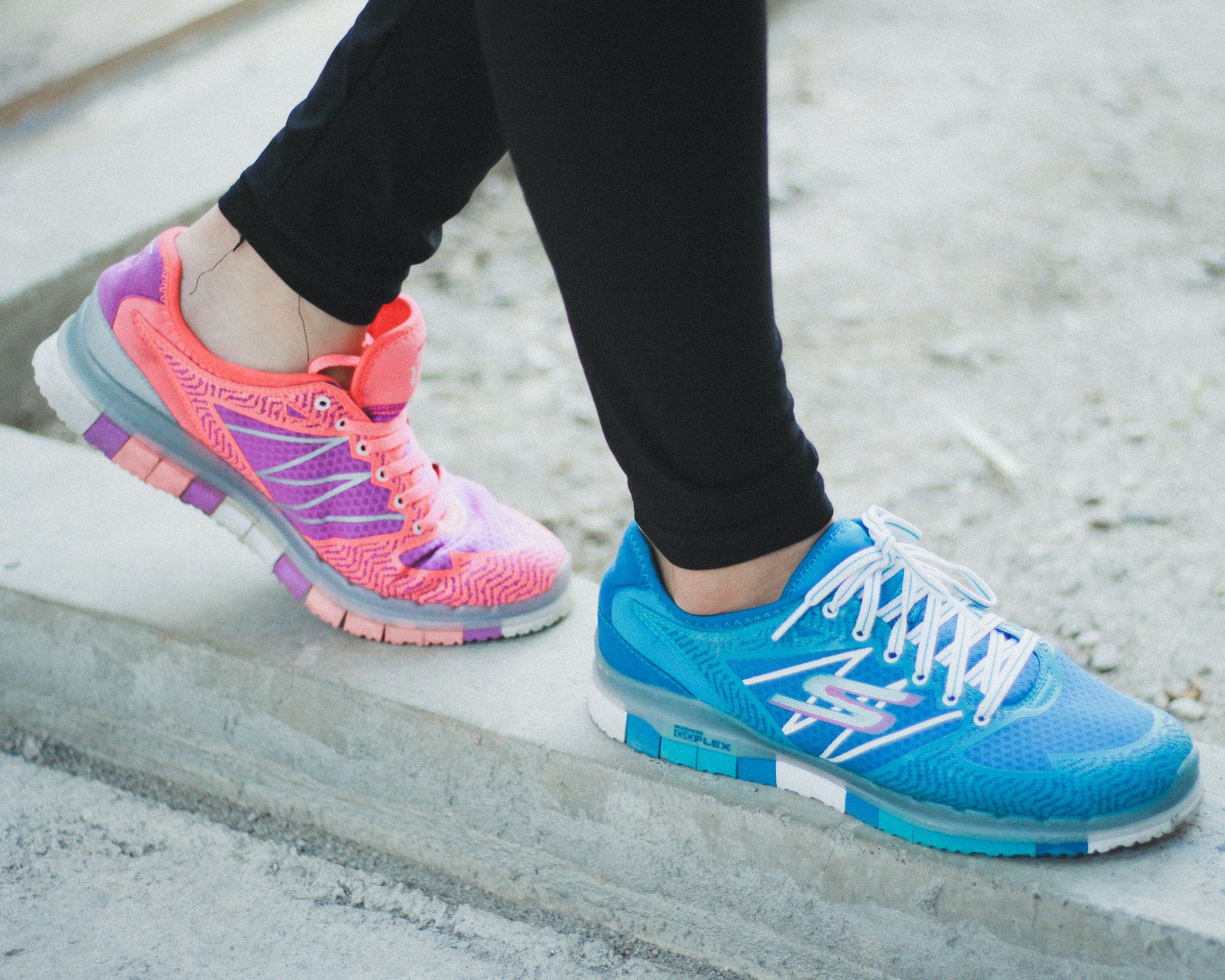 Someone walking along a concrete ledge wearing a bright blue and pink pair of Skechers sneakers.