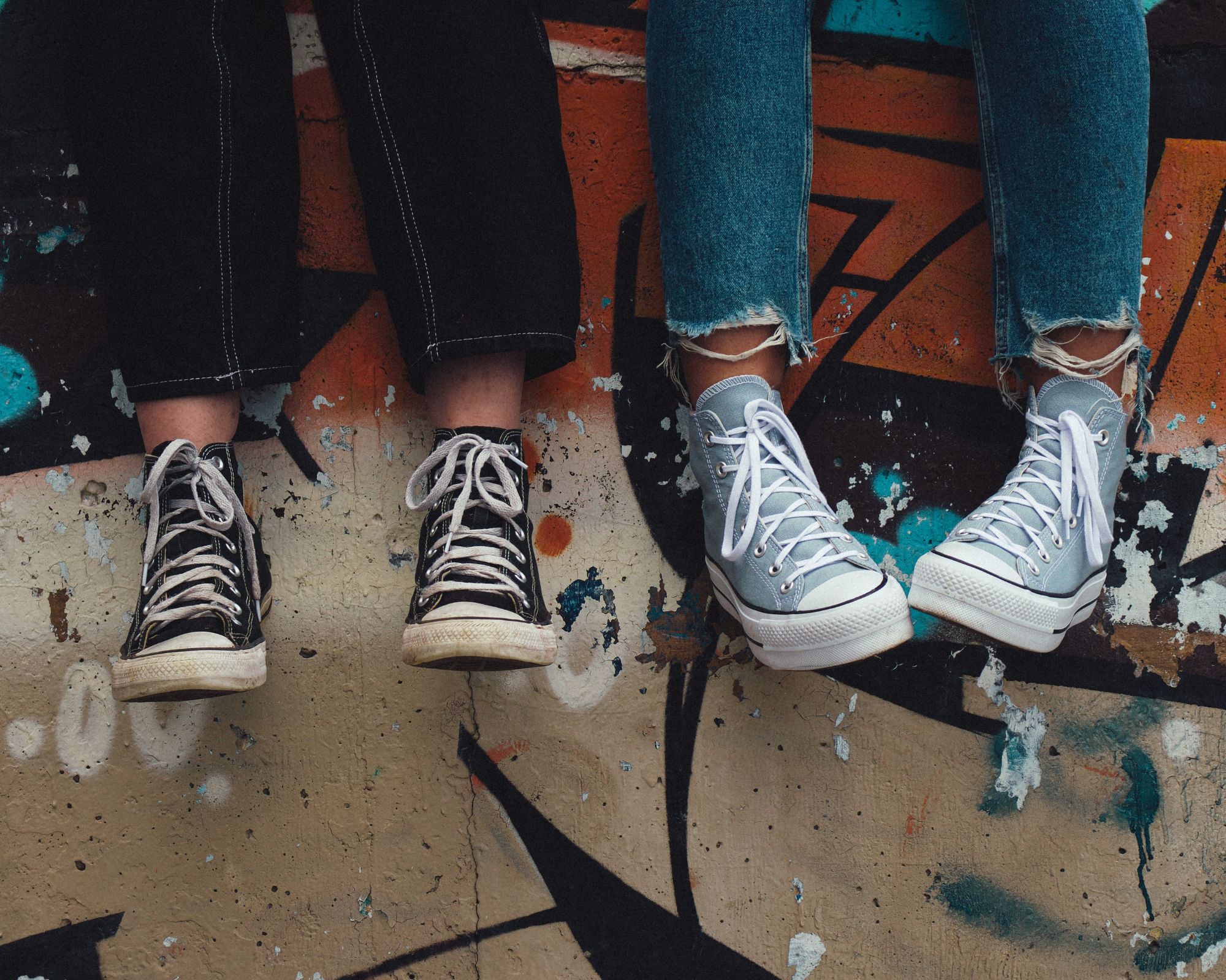 Two people sitting on a graffiti wall wearing old Converse sneakers.